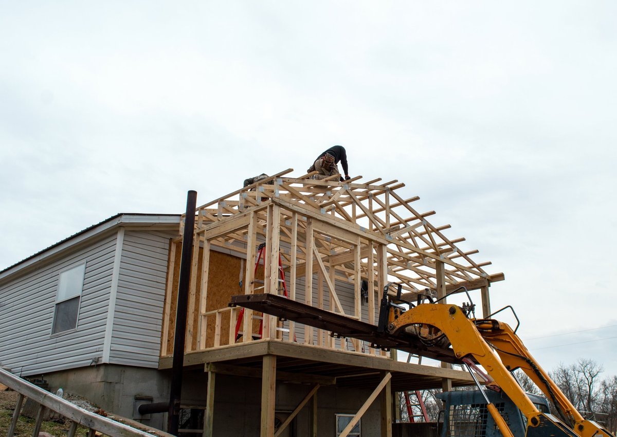 Carpenters work on new roof construction with heavy equipment at a home addition job site