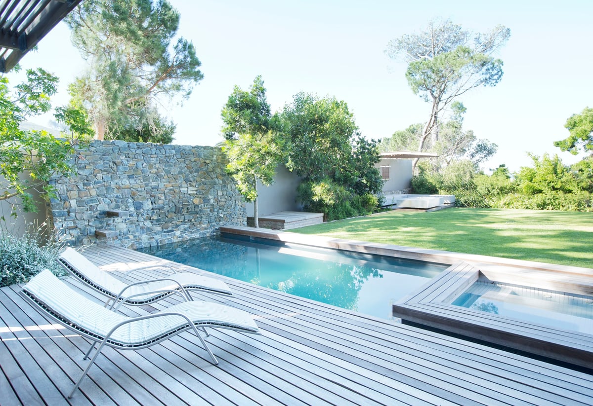 Modern patio with wooden deck, lounge chairs, rectangular pool, and lush garden