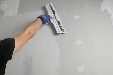 Professional worker plastering wall with putty knife, closeup