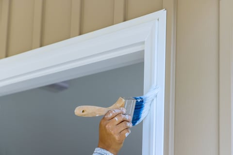 Painter using paintbrush to paint wooden moldings on door trims