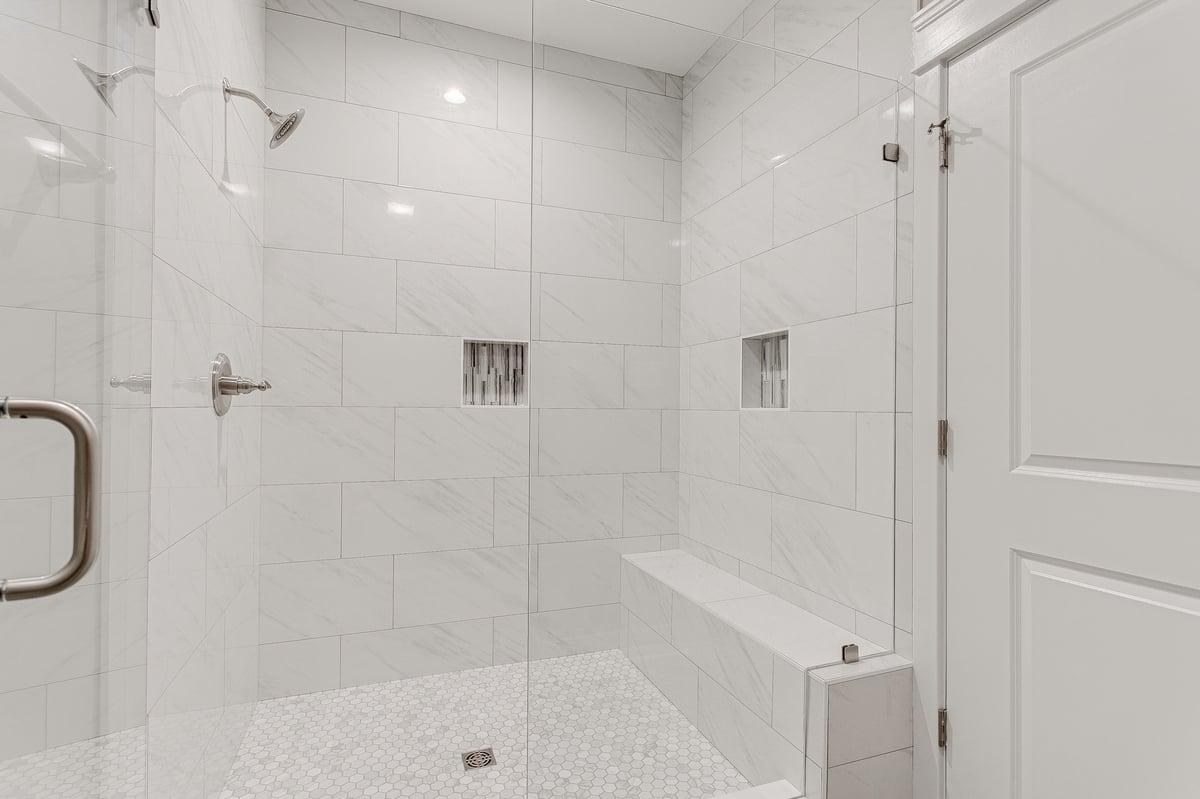 A modern glass-enclosed walk-in shower featuring white tiles, built-in benches, and niches, providing a luxurious and spacious bathing experience in a sophisticated bathroom.