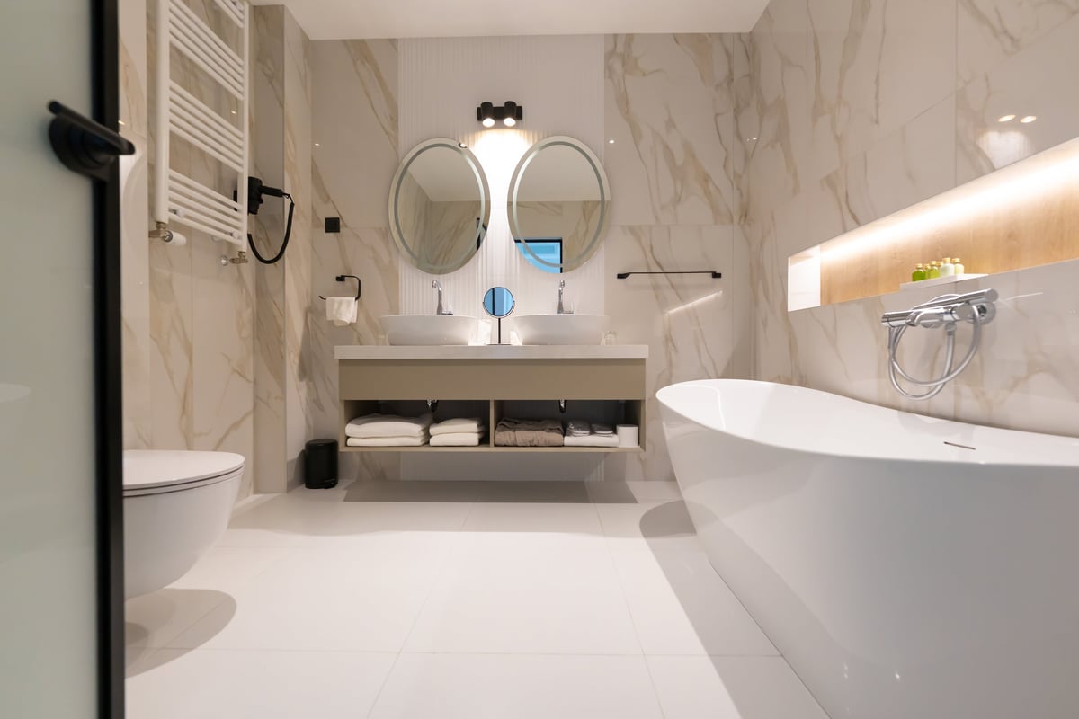A spacious modern hotel bathroom with freestanding tub, double sink, toilet and round mirrors.