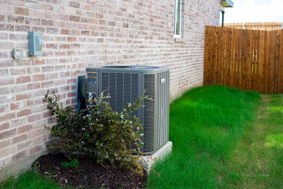 Texas summer home maintenance HVAC unit alongside modern brick home with green lawn and privacy fence