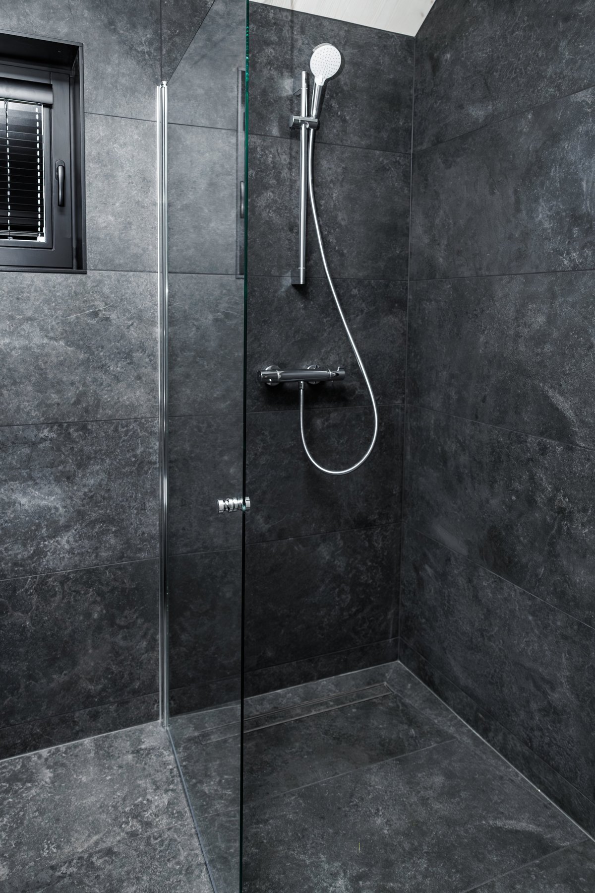 Sleek walk-in shower with chrome fixtures, glass partition, and dark grey tiles, offering a modern and elegant bathroom design with minimalist aesthetics