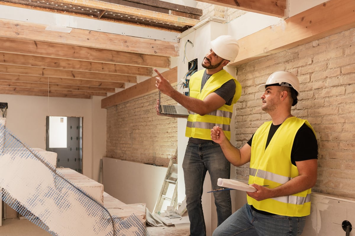 Two male Construction workers discussing renovation project with laptop and blueprints at build site