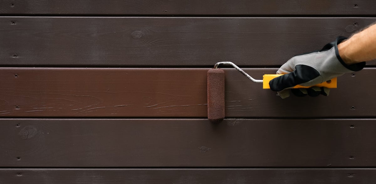 Hand with paint roller painting wooden house exterior siding