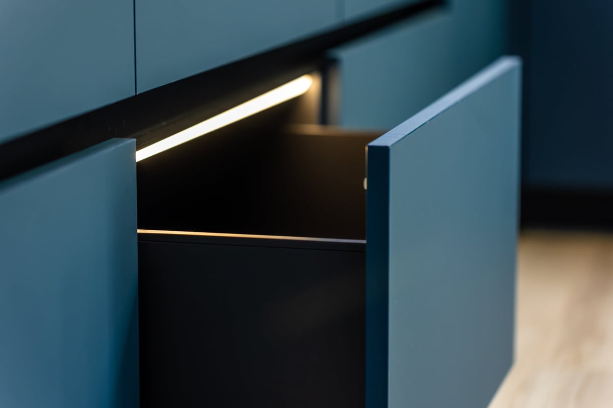 Close view of a handleless drawer lit by warm LED. Matte blue fronts and crisp lines deliver a clean, contemporary kitchen aesthetic.