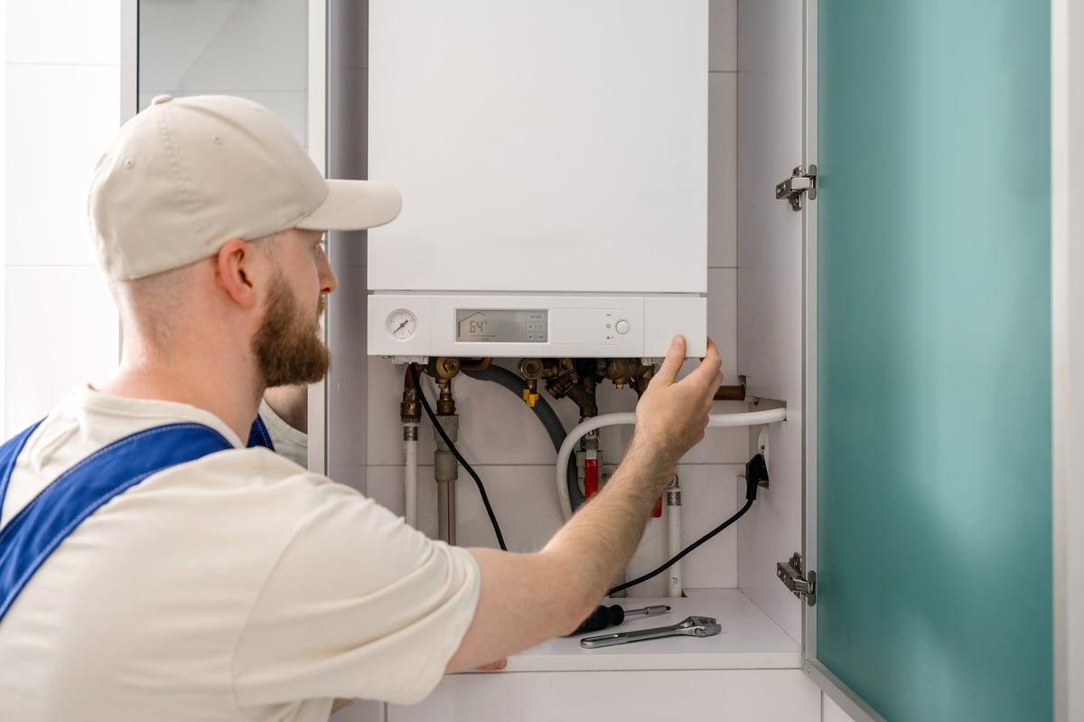 Back rear view of a repairman is inspecting a gas boiler in a bathroom, focusing on maintenance tasks to ensure optimal performance.