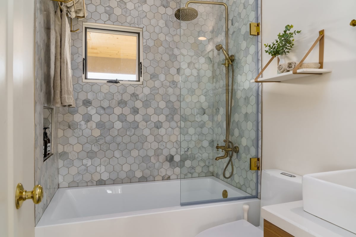 Modern bathroom in white with shower tub with hexagonal tile and gold brass fixtures