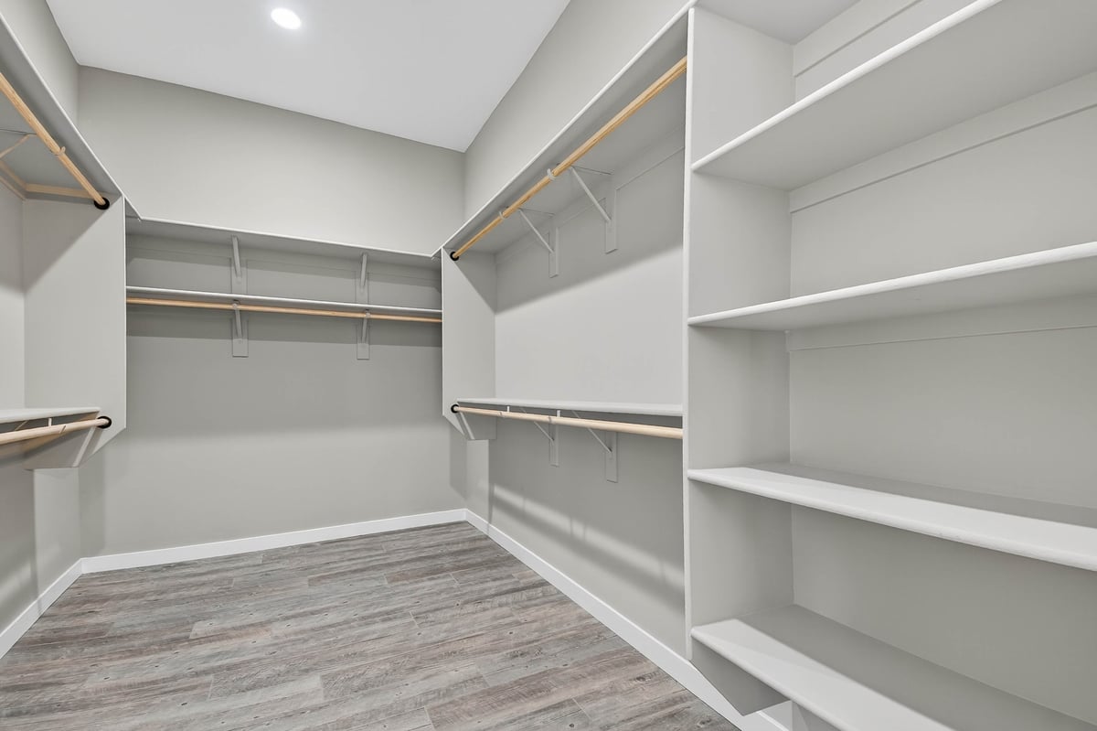 Spacious Empty Walk-In Closet With Shelves. Built-In Shelving And Hanging Rods, Wood-Look Laminate Flooring