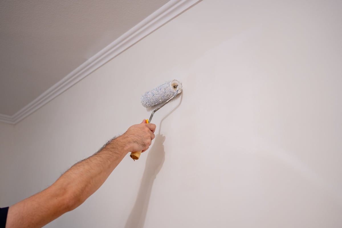 The active hand of a homeowner or professional worker performing the essential task of painting the wall during apartment maintenance and remodeling.
