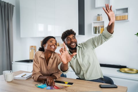 Happy black couple discussing home improvement, choosing paint colors with swatches for their new kitchen design, imagining the future of their renovated space together