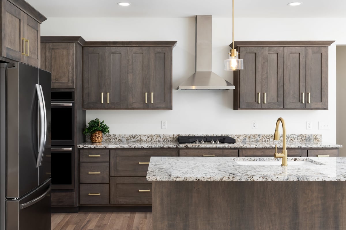 Kitchen with gold faucet on granite countertop, dark wood cabinets, stainless steel appliances, and gold pendant lights