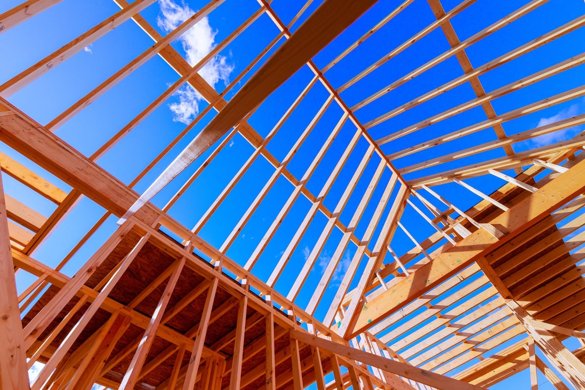 Workers are constructing wooden frame beams for new building under roof trusses