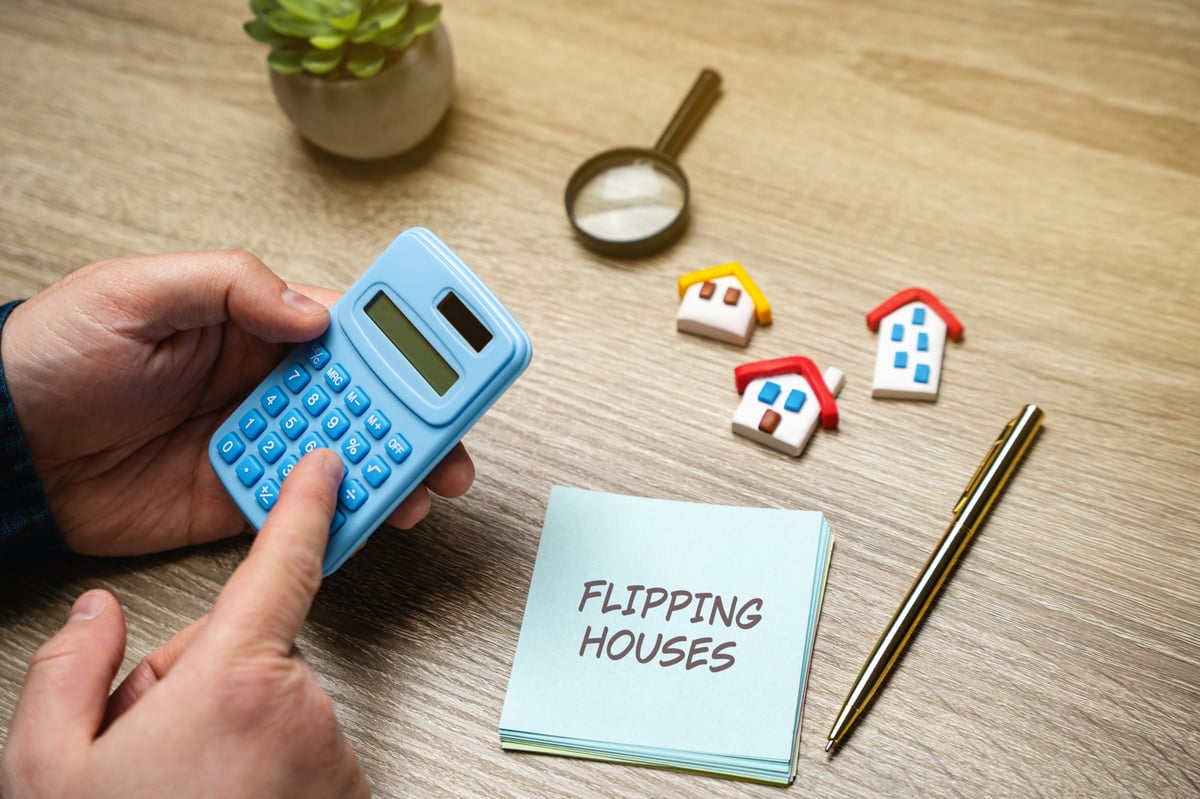 Flipping houses concept. Process of buying a property, renovating it, and then selling it for a profit. Notes with inscription and calculator in the hands of a businessman. Real estate and business