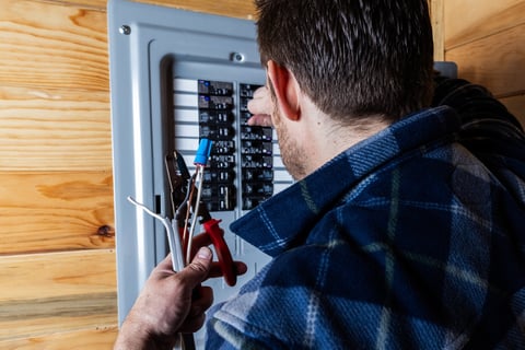Technician using wire strippers to prepare electrical cables for installation in a home circuit breaker box