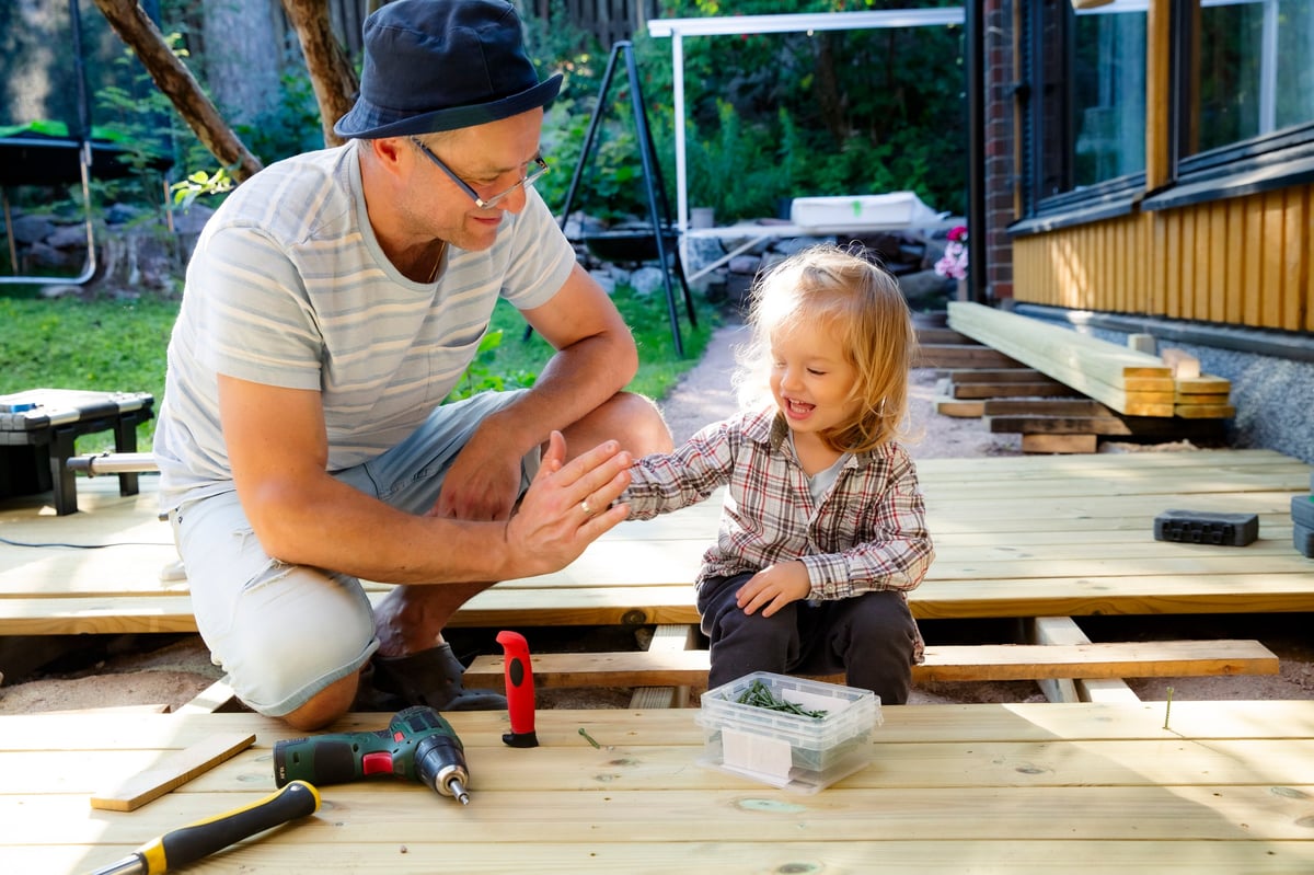 Joyful father and daughter building a wooden patio deck together. Authentic family DIY home improvement project, sunny outdoor leisure. High quality photo