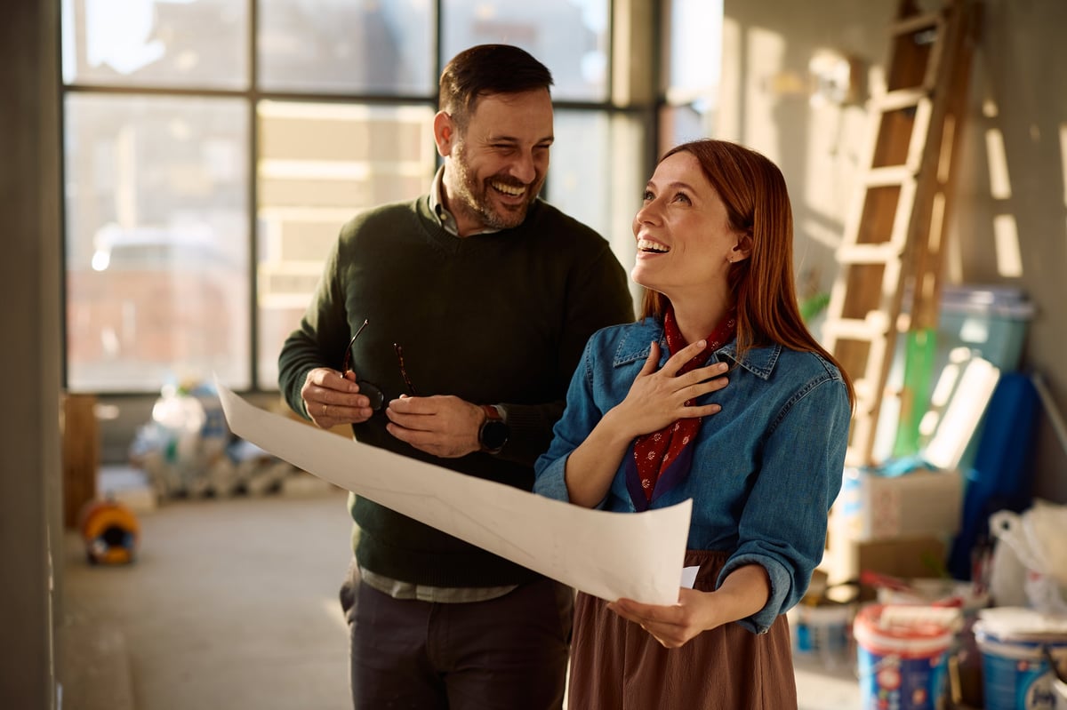 Happy couple laughing while examining blueprints during home remodeling process.