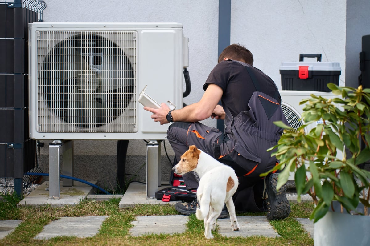 Technician servicing outdoor heat pump unit near residential building. Concept of HVAC maintenance, repair, home heating and energy efficient technology.