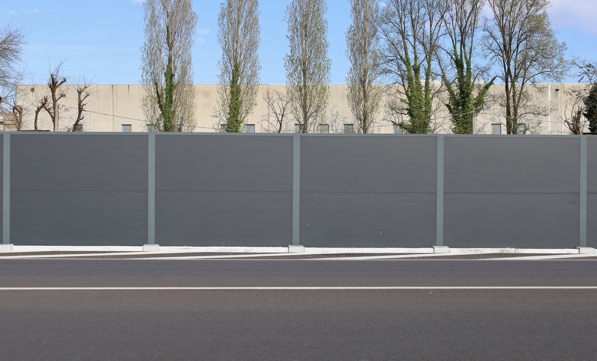 High WPC, wood-plastic composite, fence at roadside. Industrial building. trees and sky on behind. Road in front. Background for copy space.