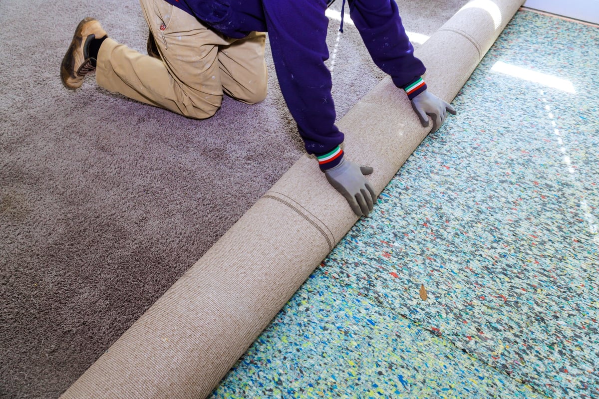 Worker is kneeling unrolling new carpet in room as part of renovation task