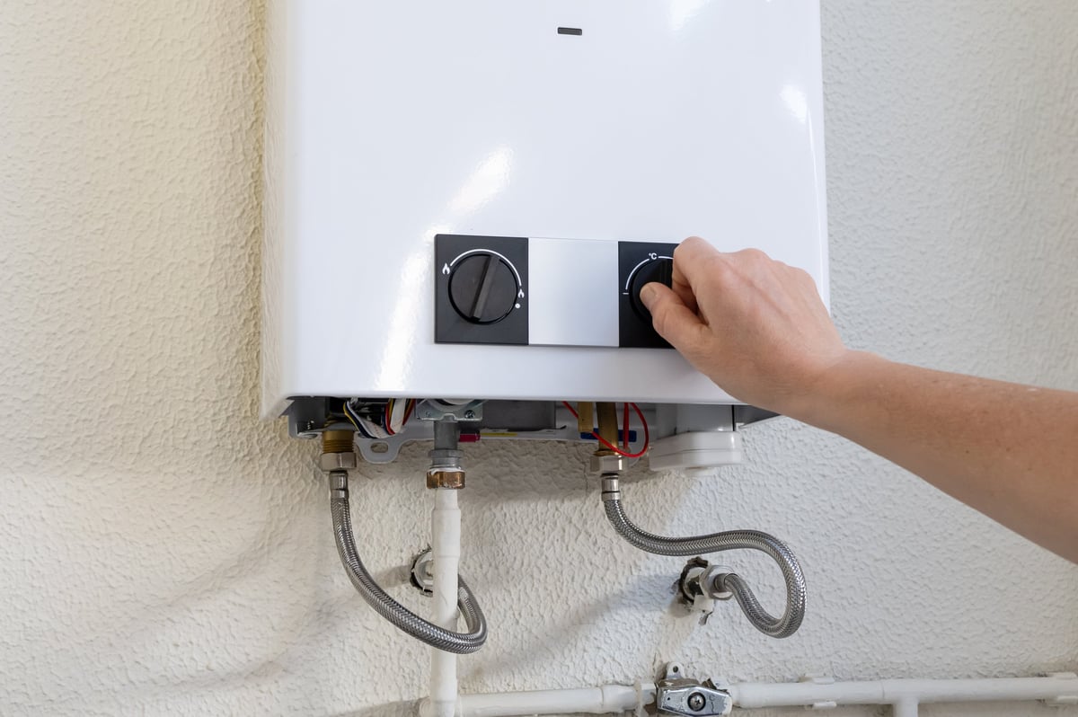 Person's hand adjusting the temperature dial on a tankless gas water heater mounted on a wall