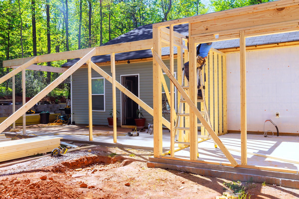 Workers install wooden beams for home extension in wooded area during trusses frame