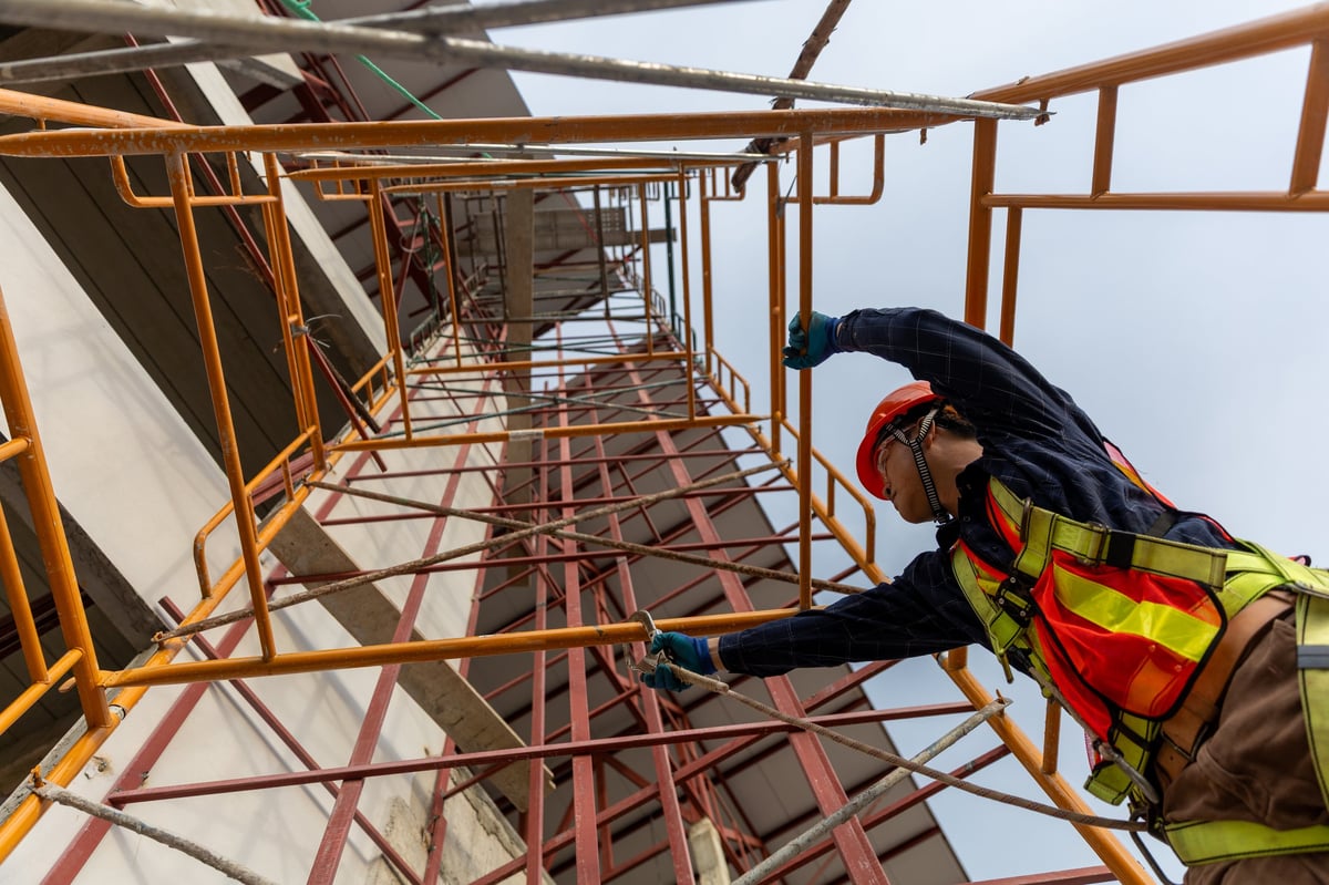 A construction worker ascends scaffolding showcasing engineering skills and safety practices on a busy building site.