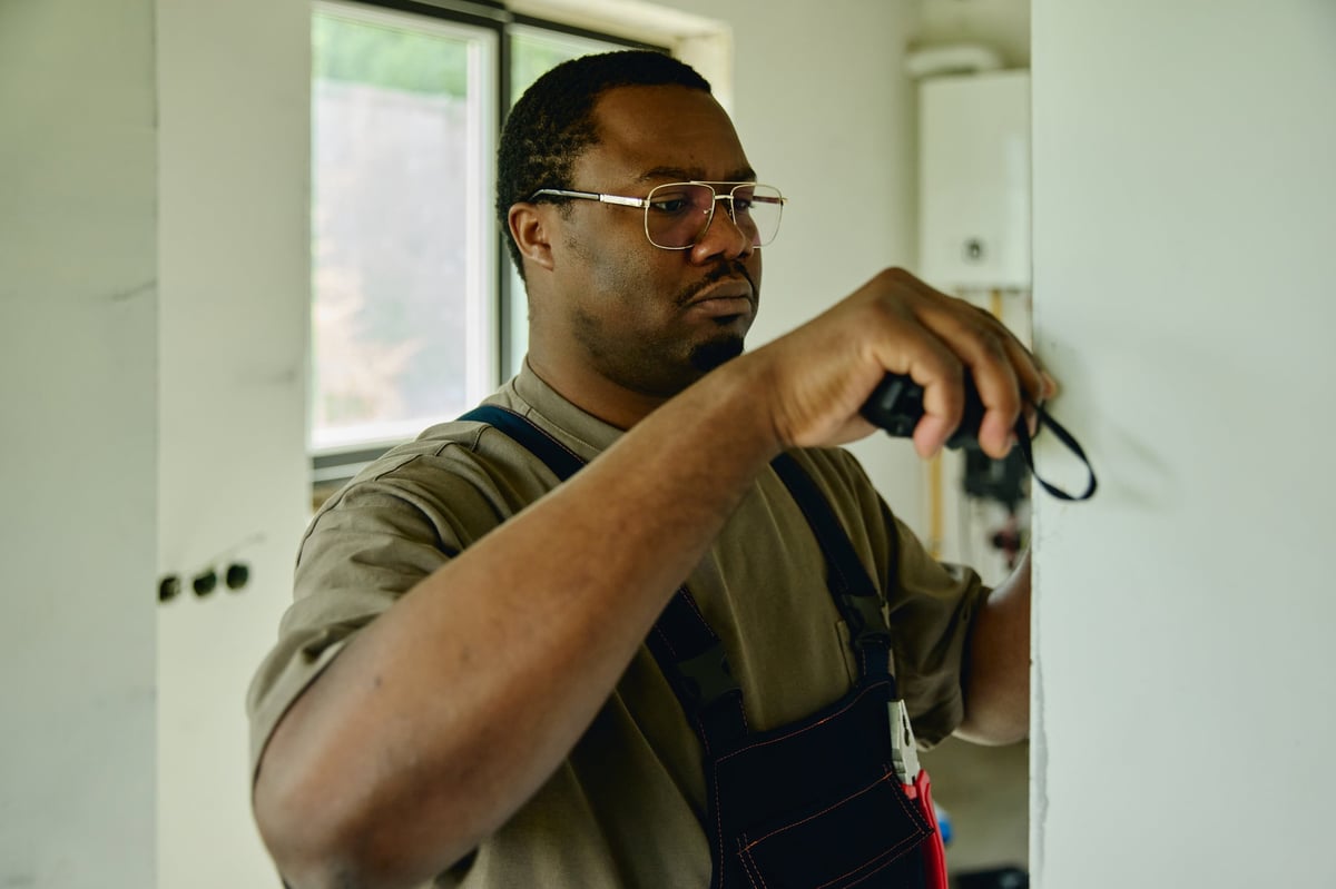 African American male contractor measuring wall during house renovation, representing home improvement services