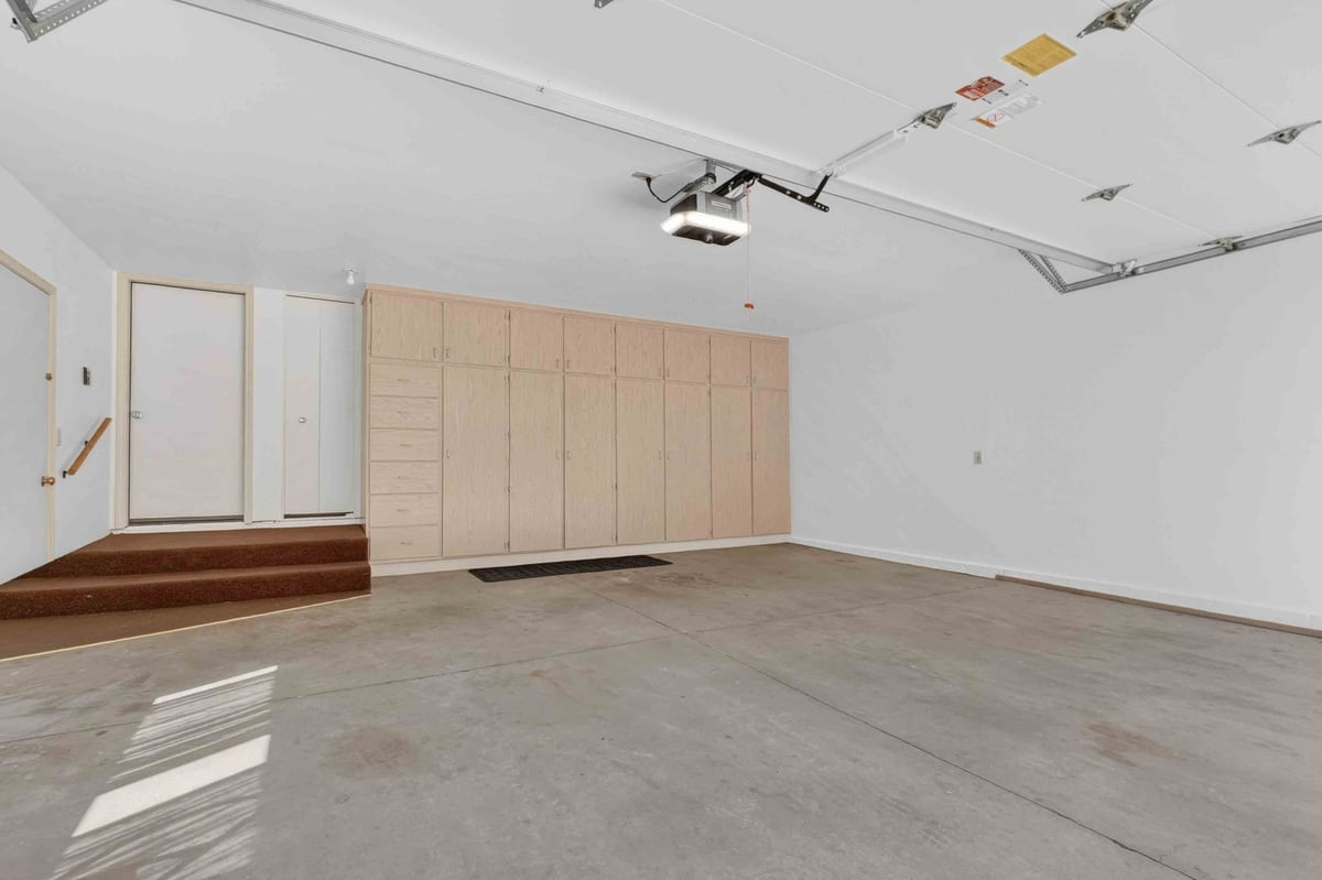 Bright garage interior with tall light wood cabinets, concrete floor, overhead door track, ceiling opener, and step entry, showing clean organized workspace now