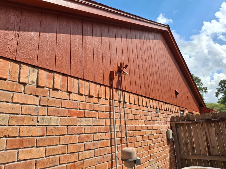 Rusty metal weathervane mounted on peak of red brick barn roof against blue sky