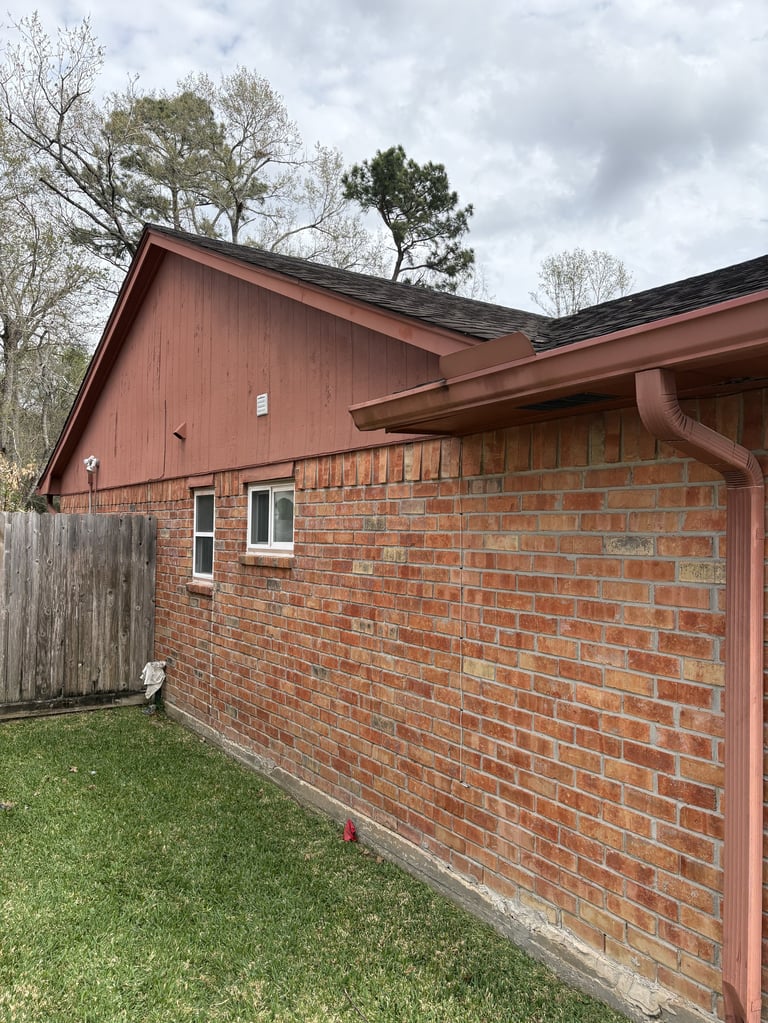 Red brick and brown metal residential house exterior with green lawn, bare trees, and overcast sky