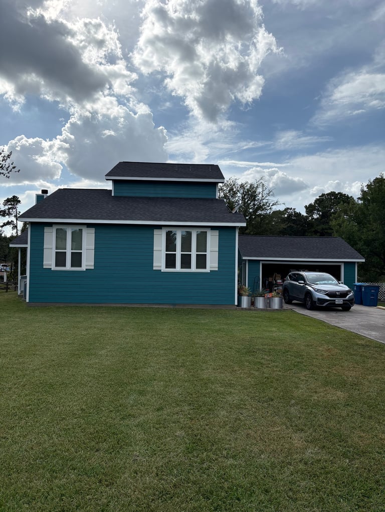 Turquoise blue house with white trim and dark roof, featuring attached carport with parked car, set on green lawn under cloudy sky