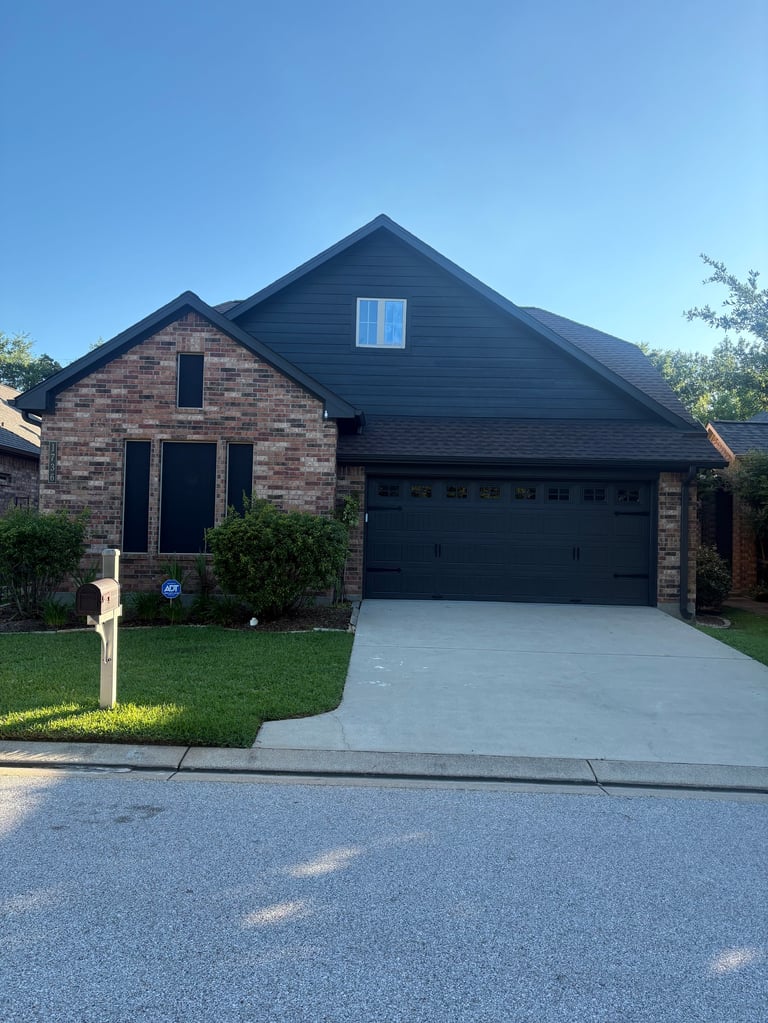 Modern brick and dark siding home with two-car garage, concrete driveway, and manicured lawn on clear sunny day - exterior rehab after