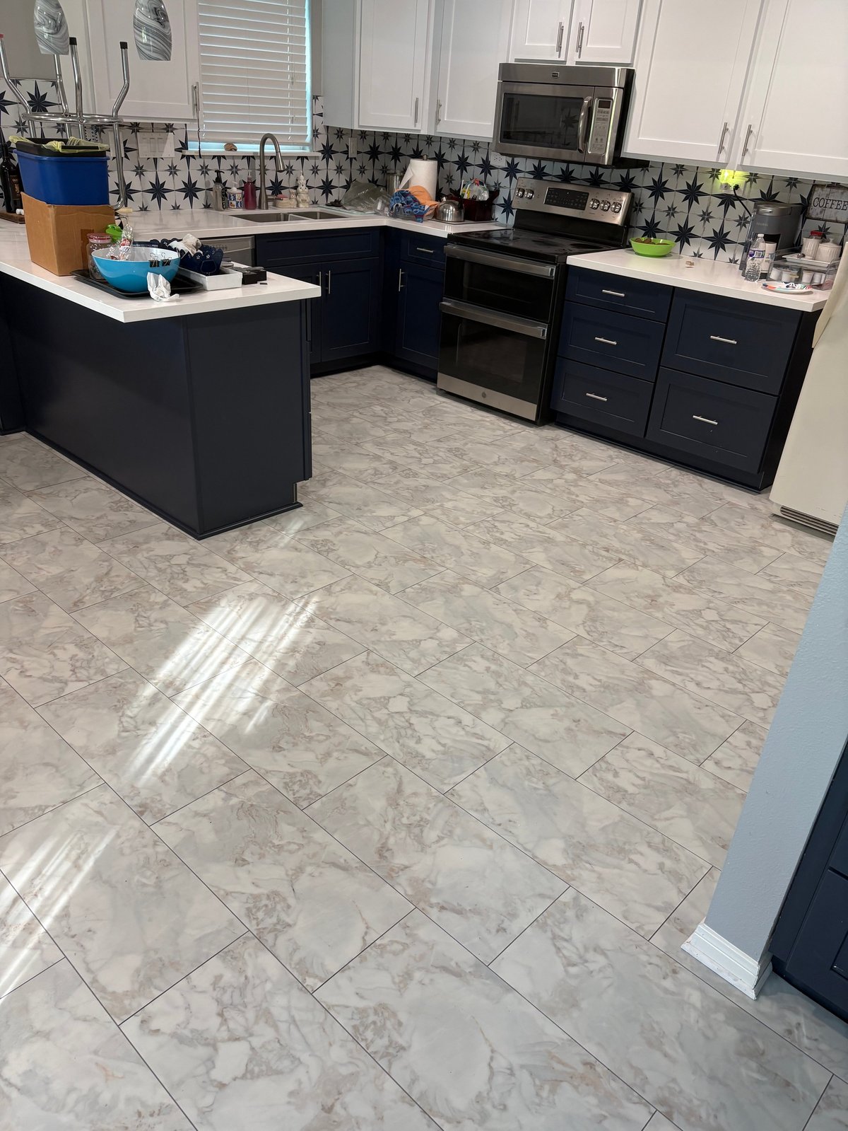 Modern kitchen with black cabinets, white upper cabinets, marble-look tile flooring, and stainless steel appliances