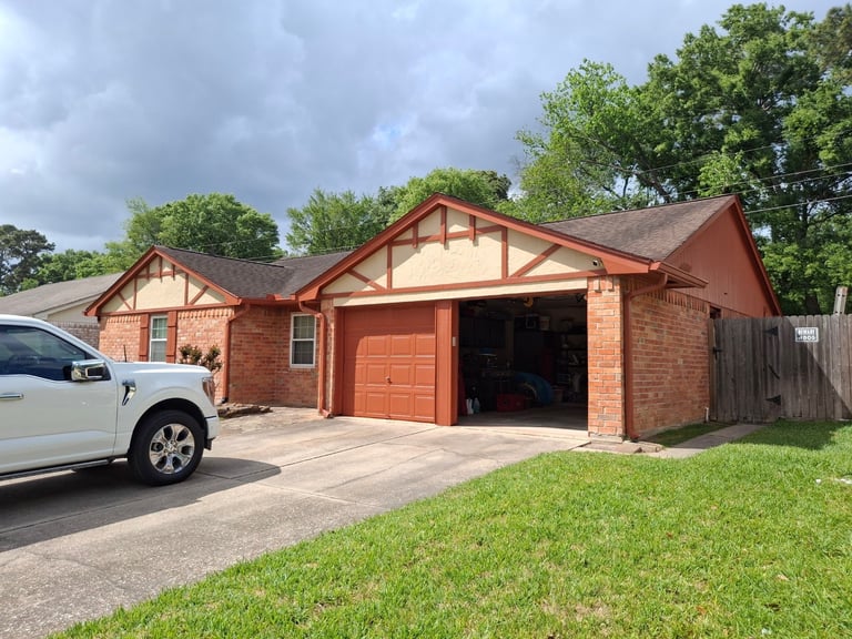 Red brick ranch-style house with open garage, white SUV in driveway, green lawn, and trees in background