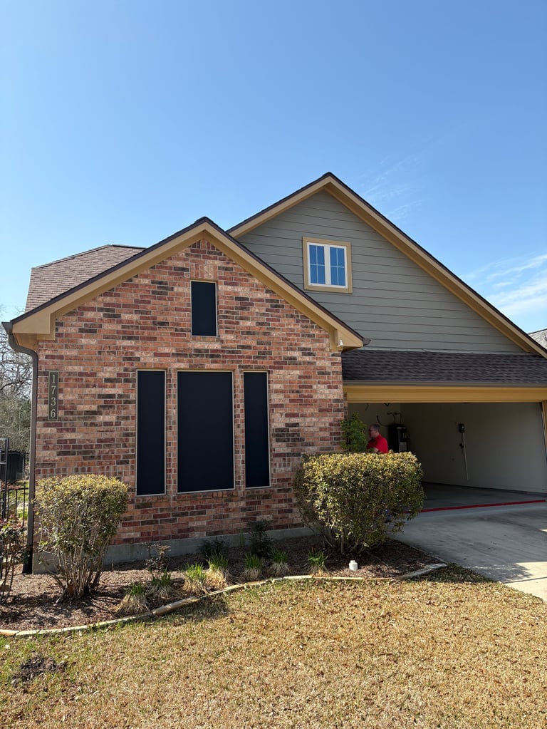 Modern brick house with attached garage, gray siding on upper level, and landscaped front yard under clear blue sky - exterior before renovation